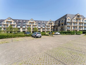 A multi-story residential building with a paved courtyard and several cars parked in front. - Goldsands III with parking by Interhome (De Haan)