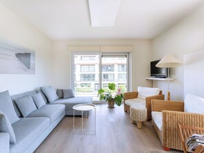 Una sala de estar moderna con un sofá gris, una mesita redonda pequeña, una silla de mimbre y una lámpara de pie.