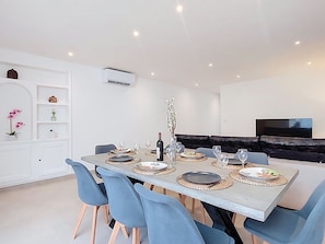A modern dining area with a rectangular table set for four, surrounded by blue chairs, and a black sofa in the background. - Maison Lou Oustaou by Interhome (Sainte Maxime)