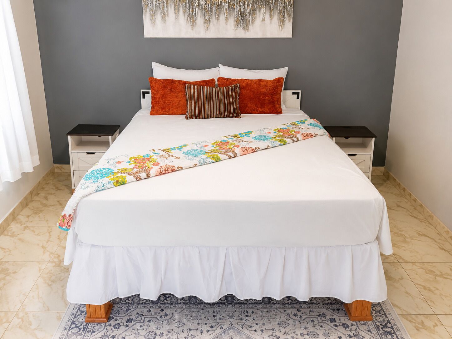 A neatly made bed with a floral bedspread, two nightstands, and a decorative wall piece.