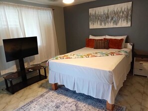 Um quarto com uma cama, televisão, um quadro e uma mesinha de cabeceira.