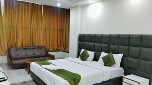 Une chambre d’hôtel avec un grand lit, un fauteuil brun, une petite table et une table de chevet avec des tiroirs.