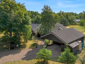 Een modern gebouw met een schuin dak, omgeven door bomen en een grindpad.