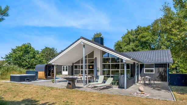 Ein modernes Haus mit großem Glasanbau, Sitzgelegenheit im Freien und einem Whirlpool.