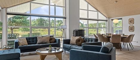 A spacious living room with large windows, a round coffee table, and a dining area with chairs.