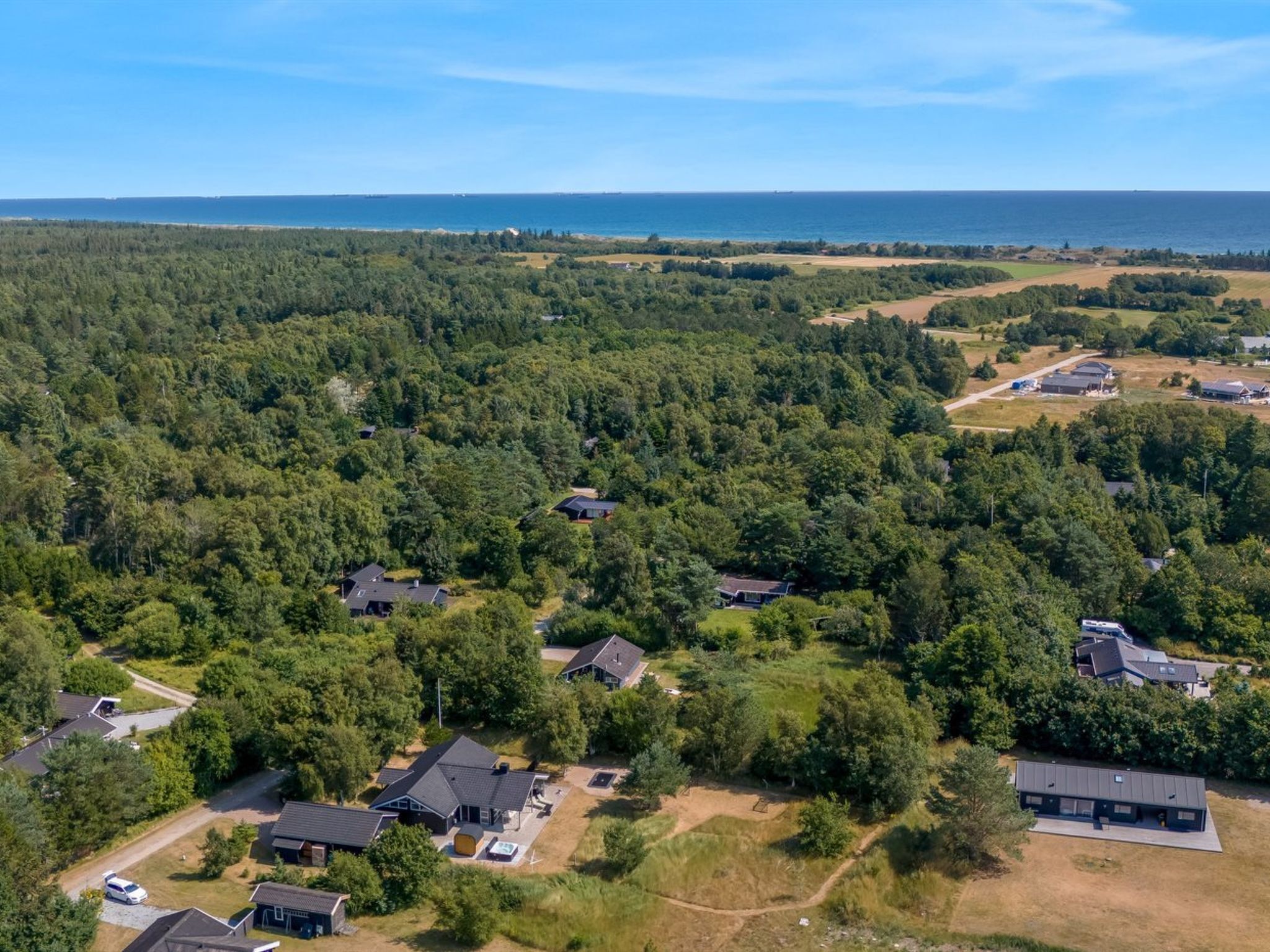 Et boligområde med flere huse omgivet af tæt skov, fri udsigt til havet og en grusvej, der forbinder ejendommene.