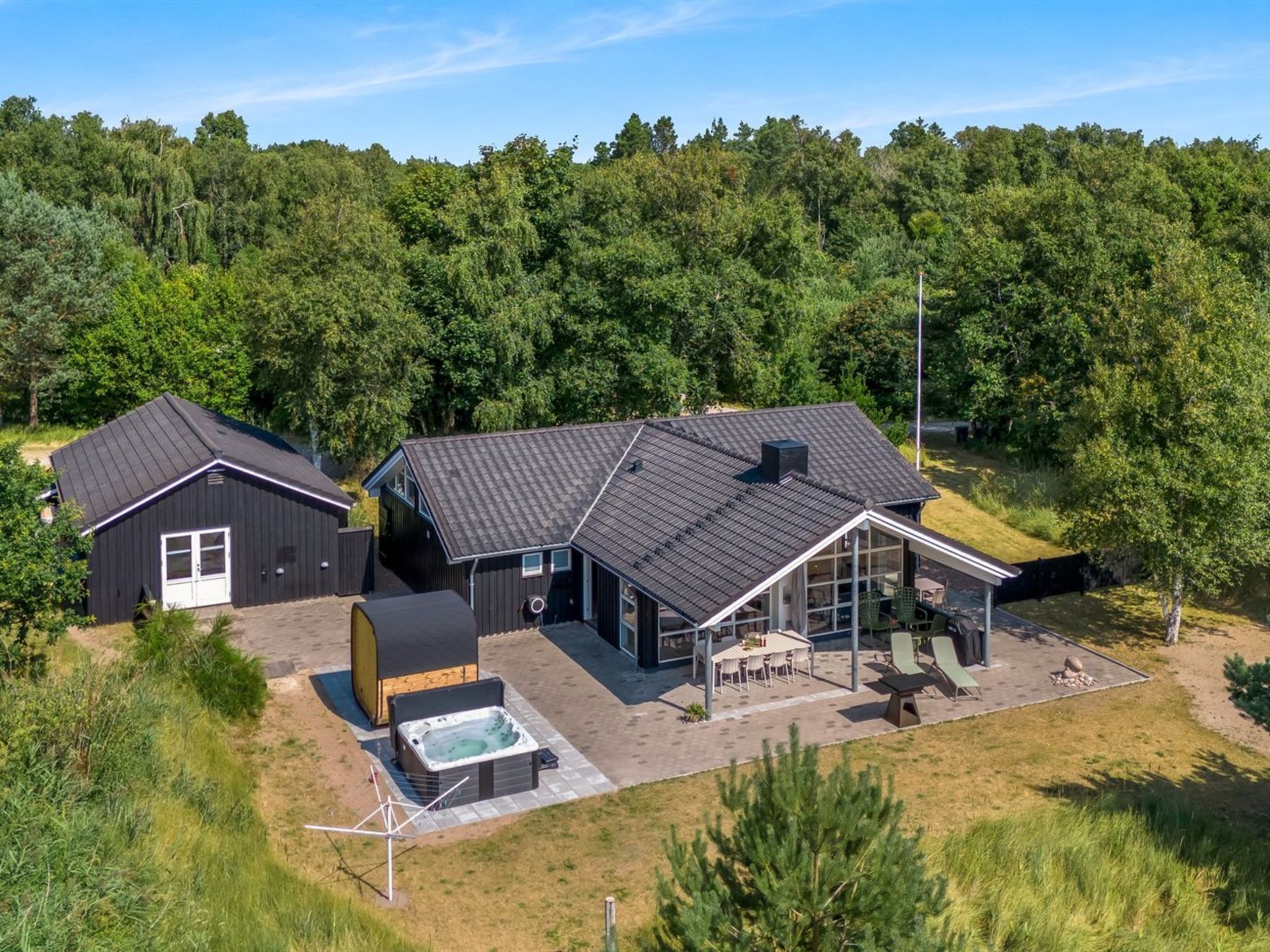 A modern two-story house with a large patio area, a hot tub, and a covered outdoor seating area.