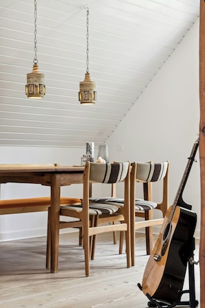 Un comedor con mesa y sillas de madera, una lámpara colgante y una guitarra apoyada en la pared.