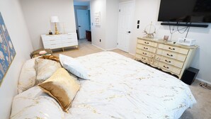 Ein Schlafzimmer mit einem großen Bett, einem Schminktisch, einem Fernseher und einer Tür zu einem weiteren Raum.