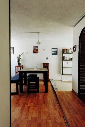 A dining area with a wooden table and chairs, a hanging light fixture, and a bookshelf with books and decorative items. - Sky · Quiet pedestrian alley · Downtown Oaxaca (Oaxaca de Juárez)