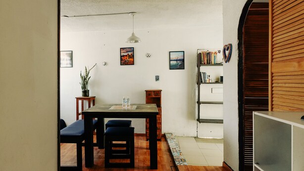 A room with a wooden dining table, two chairs, a small stool, a bookshelf, and a potted plant. - Sky · Quiet pedestrian alley · Downtown Oaxaca (Oaxaca de Juárez)