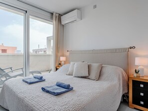 Hotelkamer met een groot bed, een raam met gordijnen, een airconditioning, een nachtkastje met een lamp, en uitzicht op gebouwen.