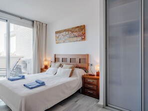 Ein Hotelzimmer mit einem großen Bett, zwei Nachttischen, einem Fenster mit Vorhängen, einem Bild an der Wand und einer Schiebetür.