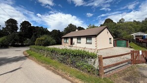 Uma casa térrea com entrada de cascalho, cerca de madeira e porta de garagem verde.