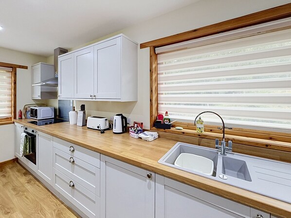 Una cocina moderna con armarios blancos, encimera de madera, horno empotrado, lavamanos y una ventana con persianas.