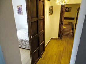 Ein Flur mit einer Holztür, einem Bett mit gemustertem Überwurf und einer Treppe, die in einen anderen Raum führt.
