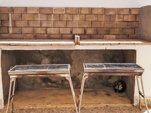 Ein Grill mit zwei Metallrosten vor einer Backsteinmauer.