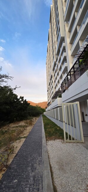 Un sendero que conduce a un edificio moderno con varios balcones y un cielo despejado.