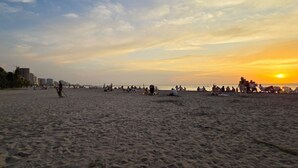Une plage avec des gens, des palmiers et des bâtiments en arrière-plan.