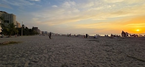 Una playa con gente, palmeras y edificios al fondo.