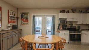 Un comedor con mesa y sillas de madera, una cocina con armarios y electrodomésticos blancos, y una puerta que da al exterior.