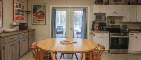 A dining area with a wooden table and chairs, a kitchen with white cabinets and appliances, and a door leading outside.