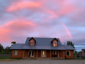 A two-story wooden house with a metal roof, a porch, and a visible front door.