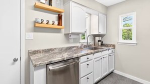 A kitchen with white cabinets, a stainless steel dishwasher, a marble countertop, and a window with a view of greenery. - Newly renovated 2-bedrm house in quiet neighborhood, close to everything! (Pittsburgh)