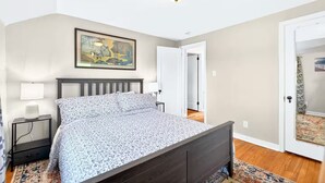 A bedroom with a bed, bedside tables, a painting, and a door leading to another room. - Newly renovated 2-bedrm house in quiet neighborhood, close to everything! (Pittsburgh)