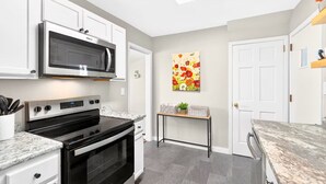 A modern kitchen with white cabinetry, a stainless steel microwave, a black oven, and a marble countertop. - Newly renovated 2-bedrm house in quiet neighborhood, close to everything! (Pittsburgh)