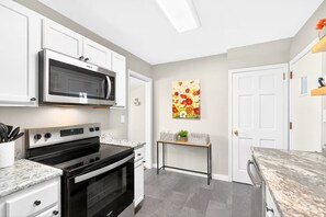 A modern kitchen with white cabinetry, a stainless steel microwave, a black oven, and a marble countertop. - Newly renovated 2-bedrm house in quiet neighborhood, close to everything! (Pittsburgh)