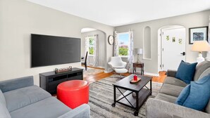 A modern living room with a flat-screen TV, a sofa, a red ottoman, and a coffee table. - Newly renovated 2-bedrm house in quiet neighborhood, close to everything! (Pittsburgh)