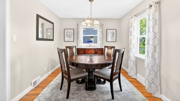 A dining room with a round table, six chairs, a chandelier, framed artwork, and a window with patterned curtains. - Newly renovated 2-bedrm house in quiet neighborhood, close to everything! (Pittsburgh)