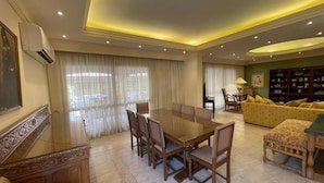 A spacious living room with a large dining table surrounded by chairs, a sofa, and a decorative cabinet. - Cozy Villa with private pool (Al Shorouk City)