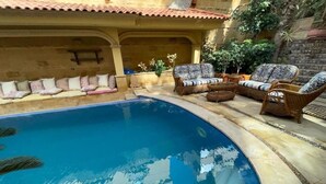 A swimming pool with a curved edge, surrounded by wicker furniture and cushions. - Cozy Villa with private pool (Al Shorouk City)