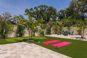 Ein Garten mit Kunstrasen, zwei Trainingsmatten, einem kleinen Pool und Gartenmöbeln.