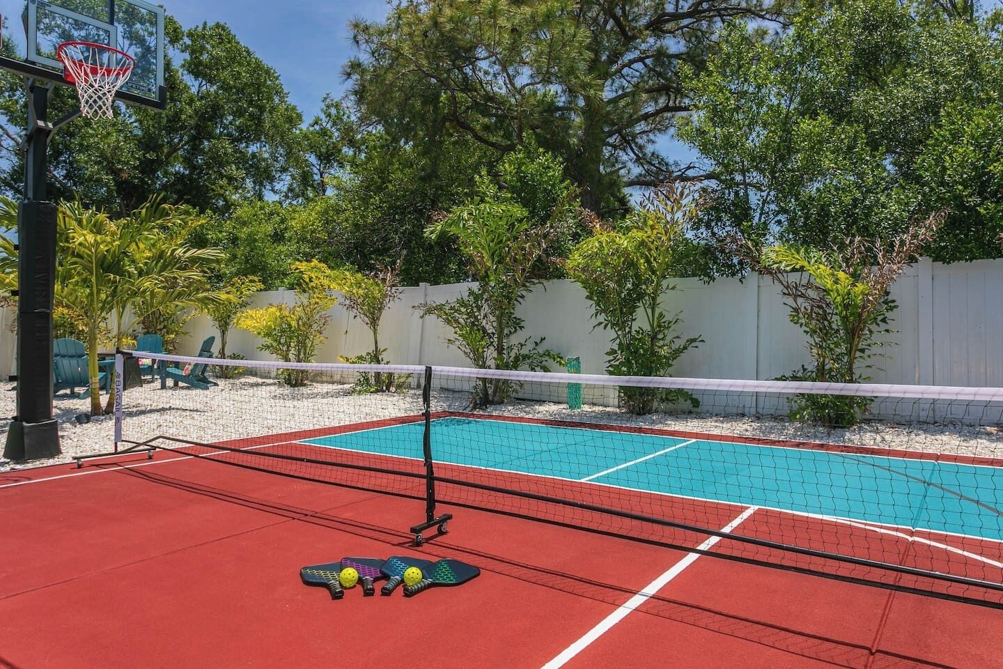 Un court de tennis avec un filet, une piscine et des sièges à l’extérieur.