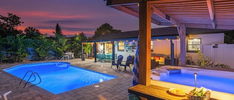 Een achtertuin met een zwembad, een jacuzzi en een overdekt terras.