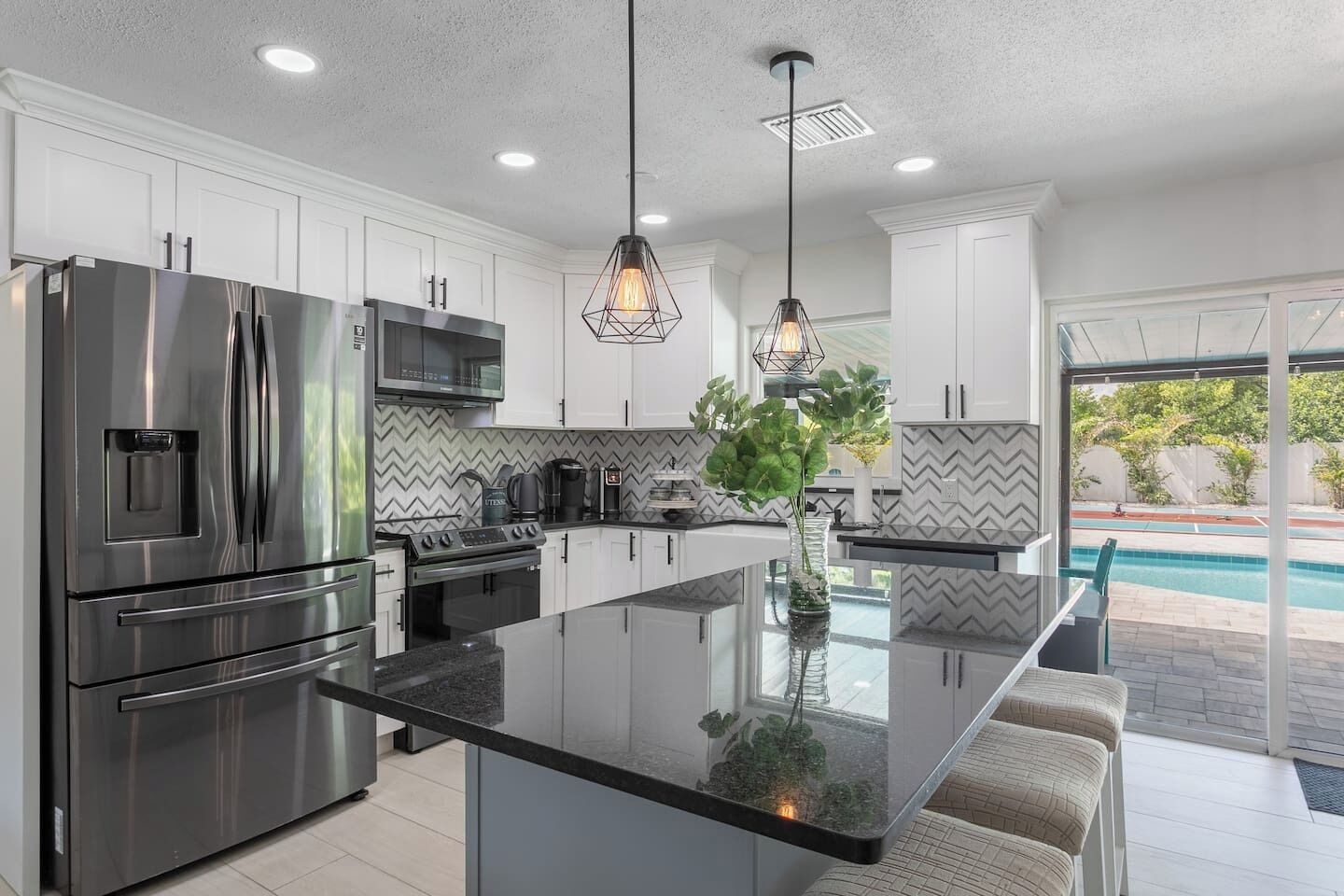 A modern kitchen with stainless steel appliances, a central island, and a view of a swimming pool.