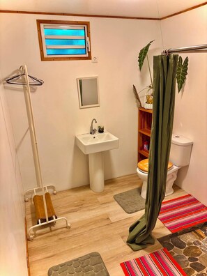 A bathroom with a white sink, a toilet, a shower curtain, a wooden floor, and a small window. - FARE AIMEHO Fully equipped bungalow. An Authentic Stay in the ❤️ of Polynesia (Moorea-Maiao)