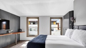 A modern hotel room with a bed, a TV, a small kitchenette, and large windows. - Skyline Studios Shoreditch (London)