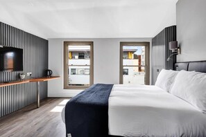 A modern hotel room with a bed, a TV, a small kitchenette, and large windows. - Skyline Studios Shoreditch (London)