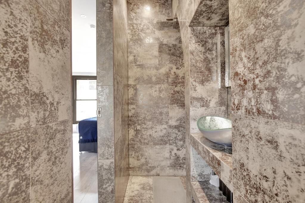 Une salle de bain avec un mur en marbre, un lavabo en forme de bol en verre et une zone de douche visible.