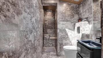 Une salle de bain avec un mur en marbre, une douche, des toilettes et un lavabo.
