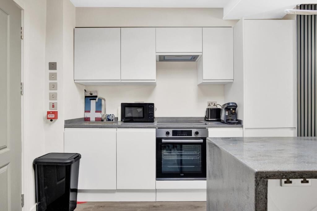 Een keuken met witte kastjes, een magnetron, een koffiezetapparaat en een oven.