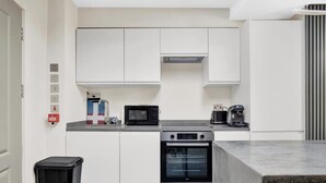 A kitchen with white cabinets, a microwave, a coffee maker, and an oven. - Skyline Studios Shoreditch (London)