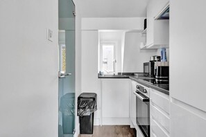 A modern kitchen with white cabinetry, a stainless steel range hood, and a built-in oven. - Skyline Studios Shoreditch (London)