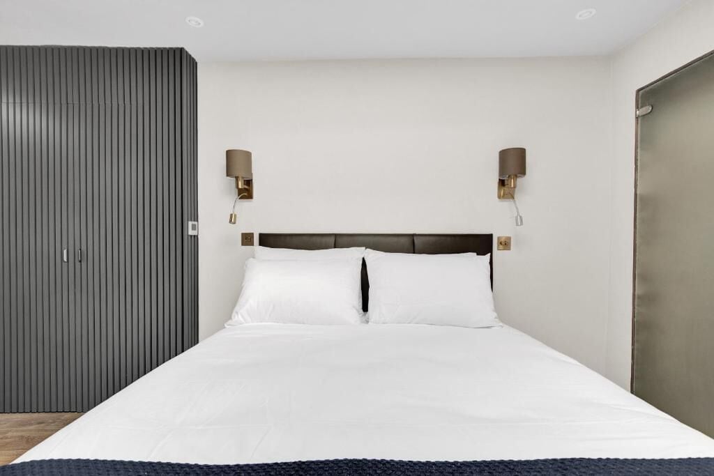 Une chambre à coucher avec un lit, deux lampes fixées au mur, une armoire et une porte.