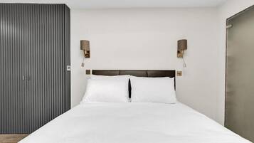 Une chambre à coucher avec un lit, deux lampes fixées au mur, une armoire et une porte.