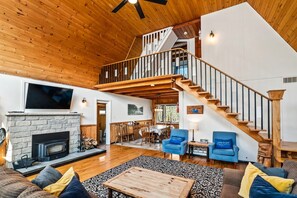 A spacious living area with a fireplace, a dining area, and a staircase leading to an upper level. - Waterfront Kawartha Lakes A Frame Cottage with Hot Tub, Pet Friendly (Kawartha Lakes)